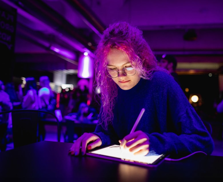 Neon lit photograph of young woman skteching on iPad while attending convention.